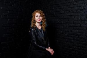 fille aux cheveux bouclés à la veste en cuir sur studio contre le mur de briques noires. photo