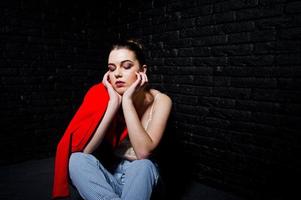 fille brune élégante sur une veste rouge contre le mur de briques noires du studio. photo