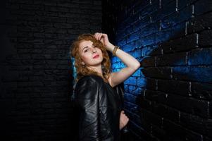 fille aux cheveux bouclés à la veste en cuir sur studio contre le mur de briques noires. photo