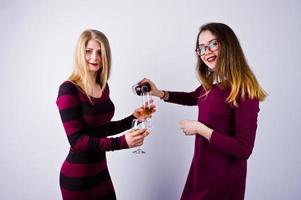 deux jolies amies en robes violettes boivent du vin mousseux ou du champagne dans le studio. photo