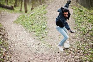 échouer en tombant d'une planche à roulettes. homme arabe de style rue à lunettes avec longboard sur bois. photo