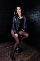 portrait en studio de fille brune sexy en veste de cuir noir contre le mur de briques. photo