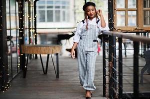 femme afro-américaine en salopette et béret posé sur une terrasse extérieure avec guirlande de décorations de noël. photo