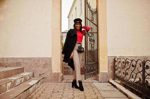 fille de mode afro-américaine en manteau et casquette de gavroche posée dans la rue. photo