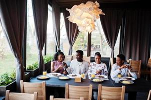 amis africains heureux assis, bavardant au café et mangeant de la nourriture. groupe de peuples noirs se réunissant au restaurant et dînant. photo