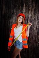 femme ingénieur en orange protège le casque et la veste de construction sur fond de bois tenant un ruban à mesurer. photo