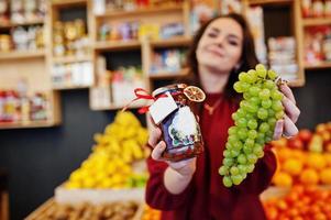 fille en rouge tenant de la confiture de raisin dans un bocal sur le magasin de fruits. photo