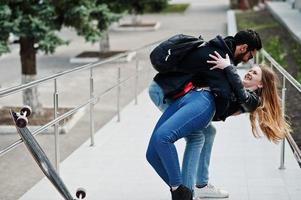 cool couple multiracial posant avec longboard et câlins ensemble. photo