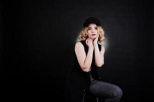 portrait en studio d'une fille blonde en vêtements noirs, soutien-gorge et casquette sur fond sombre. photo