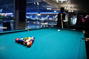 jeune bel homme africain vêtu d'une chemise blanche, d'un gilet noir et d'un nœud papillon jouant au billard. photo