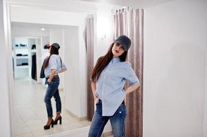 brune magnifique fille dans la boutique de vêtements décontractés et casquette contre miroir. photo