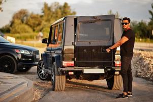 l'homme asiatique porte sur tout le noir posé près de la voiture suv, porte arrière ouverte. photo