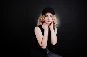 portrait en studio d'une fille blonde en vêtements noirs, soutien-gorge et casquette sur fond sombre. photo