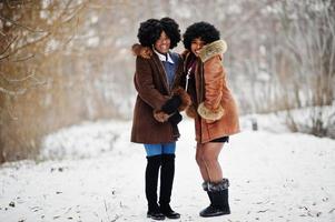 deux femmes afro-américaines aux cheveux bouclés portent un manteau et des gants en peau de mouton posés le jour de l'hiver. photo