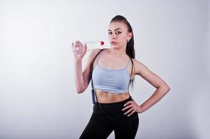 Cheerful attractive young fitness woman in top et leggings noirs avec corde à sauter et bouteille d'eau isolé sur fond blanc. photo