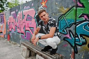 portrait de style de vie d'un bel homme posant dans la rue de la ville avec un mur de graffitis. photo