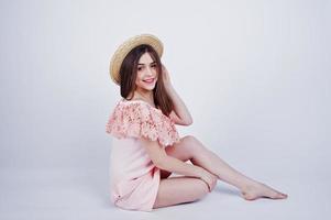 portrait d'une femme à la mode en robe rose assise et posant avec un chapeau sur le sol dans le studio. photo