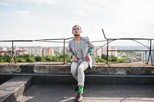 homme macho élégant rêveur en costume gris, chapeau et lunettes posés sur le toit. photo