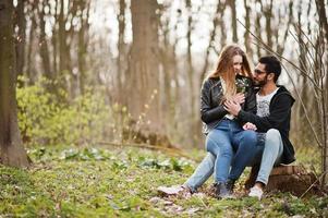 histoire d'amour d'un couple multiracial cool dans la forêt printanière. ils sont assis sur une souche. photo