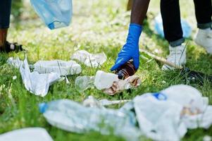 main d'un homme afro-américain ramassant une bouteille dans des sacs à ordures pendant le nettoyage de la zone dans le parc. concept de volontariat, de charité, de personnes et d'écologie en afrique. photo