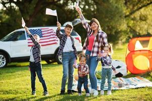 famille américaine passer du temps ensemble. avec des drapeaux américains contre une grosse voiture suv en plein air. photo