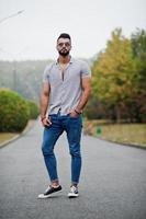 l'homme à la barbe arabe à la mode porte une chemise, un jean et des lunettes de soleil posés sur le parc et tient le portefeuille à portée de main. photo