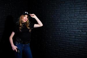 agent féminin du fbi en casquette et avec arme à feu au studio contre un mur de briques sombres. photo