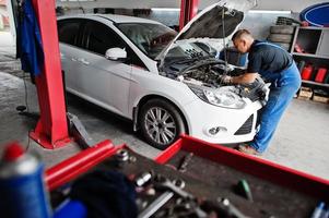 thème de la réparation et de l'entretien des voitures. mécanicien en uniforme travaillant dans le service automobile, vérifiant le moteur. photo