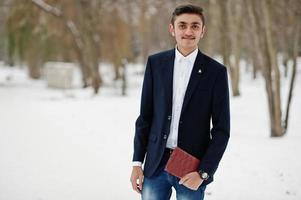 homme étudiant indien élégant en costume posé à la journée d'hiver en plein air avec un ordinateur portable à portée de main. photo