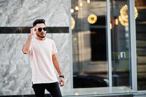 homme barbe indien élégant à lunettes de soleil et t-shirt rose. modèle indien posé en plein air dans les rues de la ville. photo