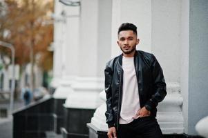 homme barbe indien élégant à la veste en cuir noir. modèle indien posé en plein air dans les rues de la ville. photo