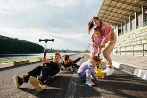 jeune mère élégante avec quatre enfants en plein air. la famille sportive passe du temps libre à l'extérieur avec des scooters et des patins. photo