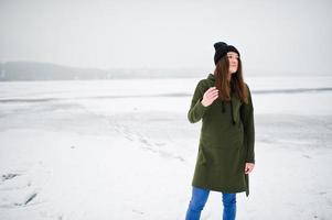 fille drôle portant un long sweat-shirt vert, un jean et un couvre-chef noir, au lac gelé en hiver. photo