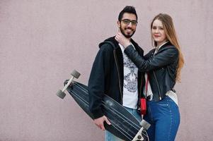 cool couple multiracial posant contre un mur rose avec longboard. photo