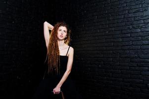 tournage en studio d'une fille en noir sur une chaise avec des dreads sur fond de brique. photo