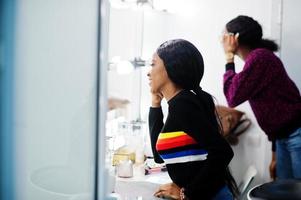 femme afro-américaine se maquillant par une maquilleuse au salon de beauté. photo