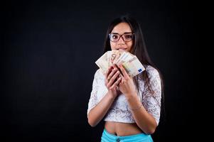 portrait d'une jolie fille en t-shirt bleu ou turquoise, pantalon et lunettes posant avec beaucoup d'argent à la main. photo