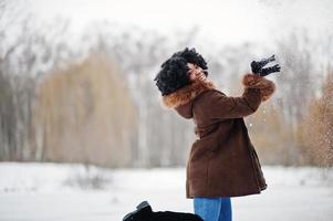 cheveux bouclés femme afro-américaine porter sur un manteau en peau de mouton et des gants posés à la journée d'hiver jette de la neige. photo