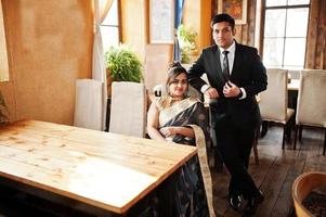 couple d'amis indiens élégants et à la mode de femme en sari et homme en costume posé café intérieur. photo