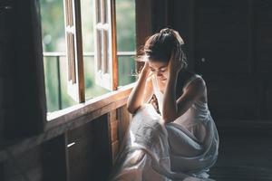 triste femme asiatique portant une robe blanche souffrant de dépression insomnie éveillée et assise seule sur le lit dans une chambre vintage. le harcèlement sexuel et la violence contre les femmes. photo