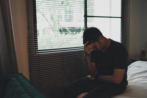 homme asiatique triste souffrant d'insomnie dépressive éveillé et assis seul sur le lit dans la chambre. silhouette homme déprimé tristement assis sur le lit dans la chambre à coucher, concept de dépression photo