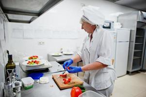 chef féminin préparant une salade dans la cuisine du restaurant italien. photo