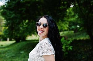 fille brune en blouse blanche avec des lunettes de soleil posées au parc. photo