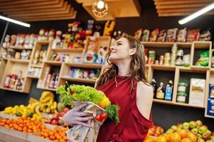 fille en rouge tenant différents légumes sur le magasin de fruits. photo