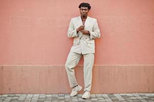 homme afro élégant en costume beige old school contre le mur rose. jeune homme africain à la mode en veste décontractée sur torse nu. photo