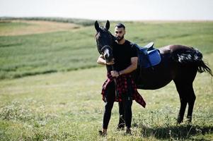 homme arabe à barbe haute en noir avec cheval arabe. photo