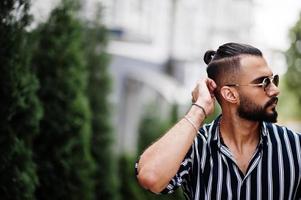 l'homme arabe réussi porte une chemise rayée et des lunettes de soleil pose en plein air. photo