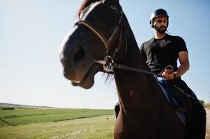 homme arabe à grande barbe portant un casque noir, monter à cheval arabe. photo