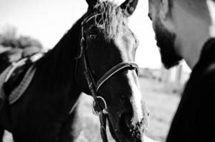 homme arabe à barbe haute en noir avec cheval arabe. photo