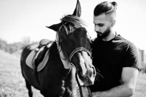 homme arabe à barbe haute en noir avec cheval arabe. photo